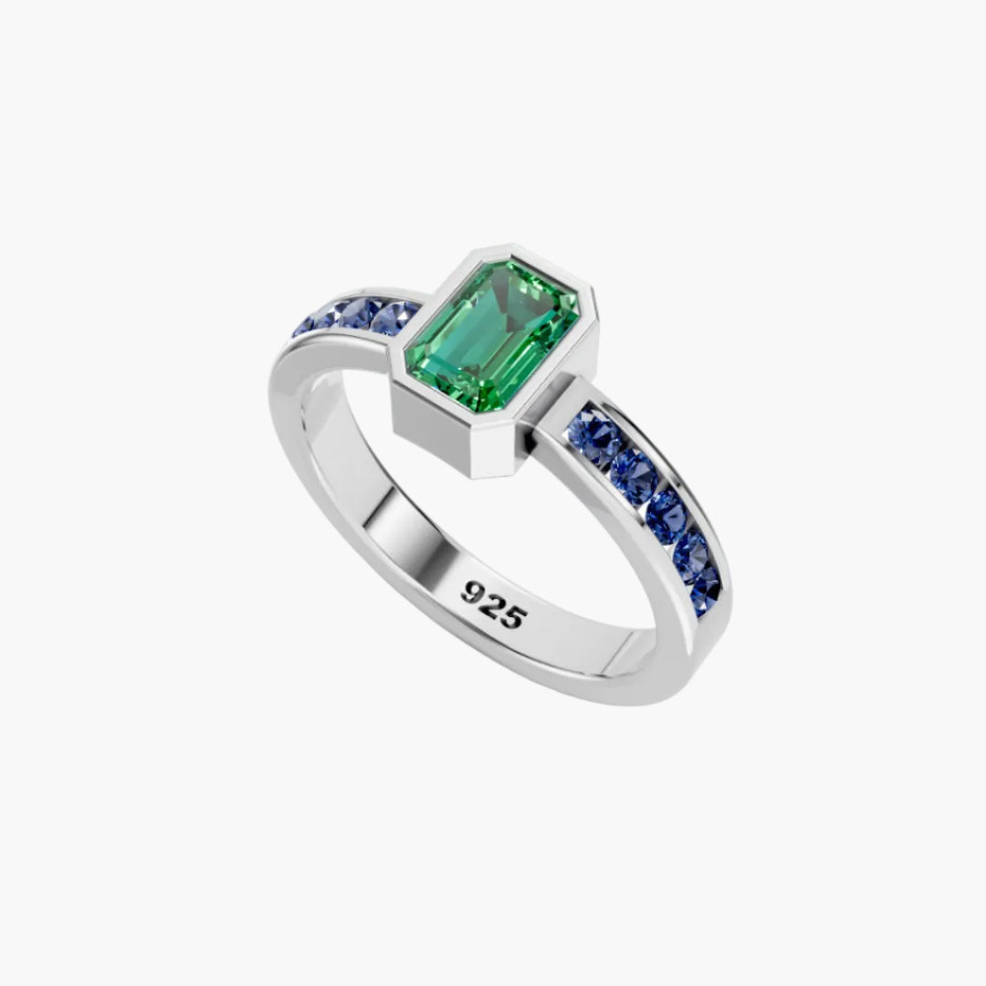 Silver ring with green gemstone and blue sapphires on a white background
