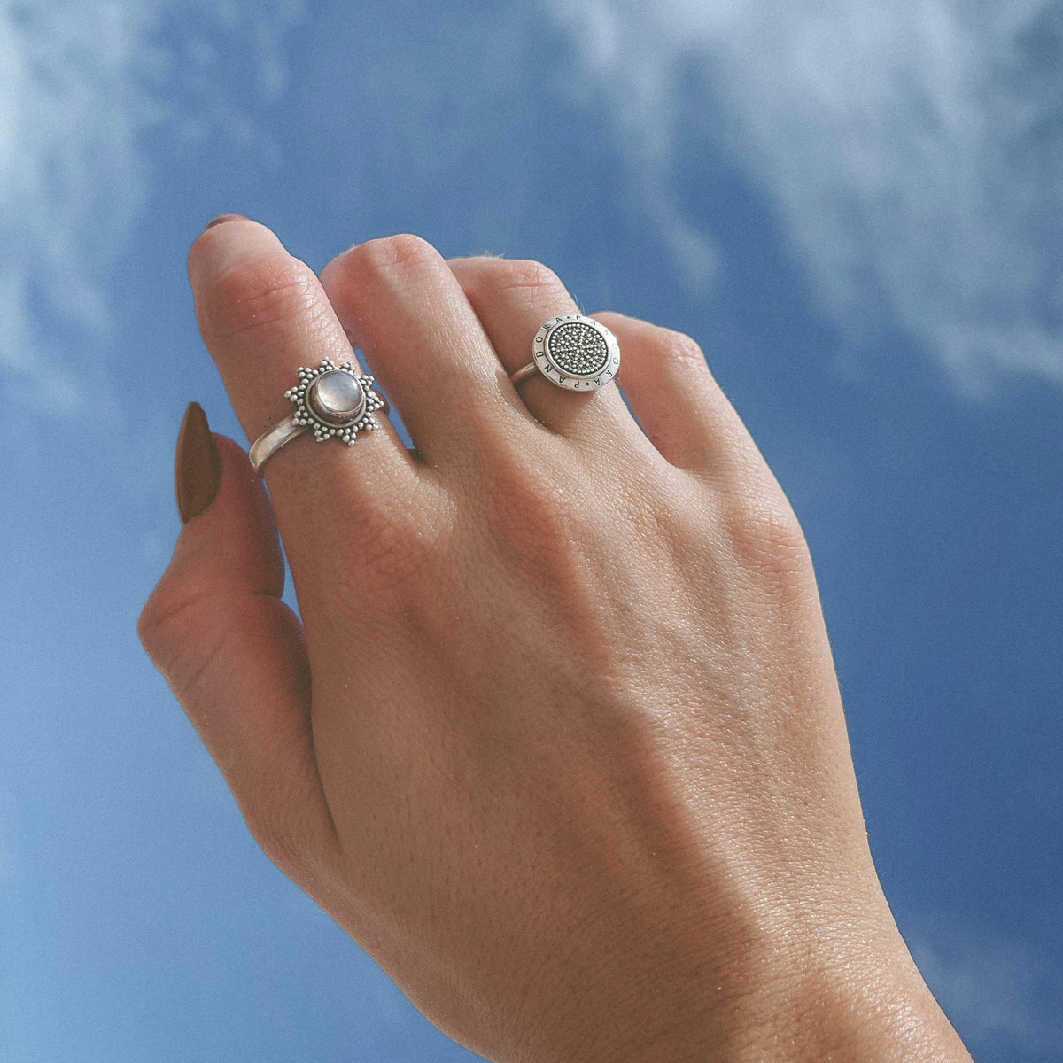 Hand wearing two silver rings against a blue sky background