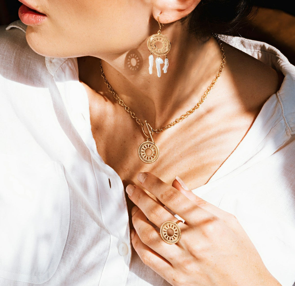 Close-up of a person wearing gold jewelry including a necklace, earrings, and ring.