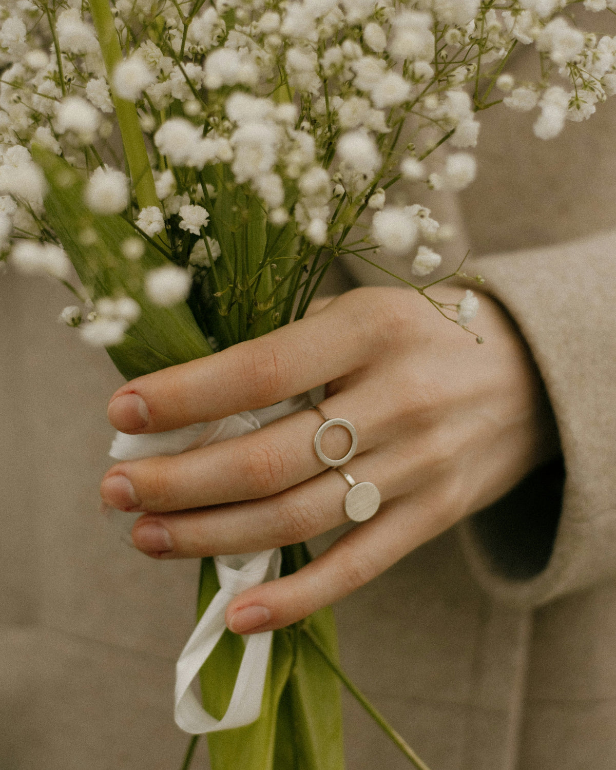 Hand holding a bouquet of small white flowers with a beige background